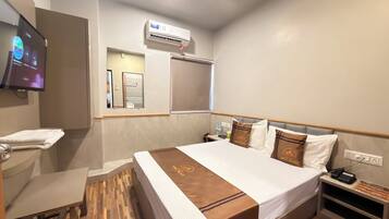 Habitación de hotel con cama, televisor, aire acondicionado, espejo, mesita de noche y velador.