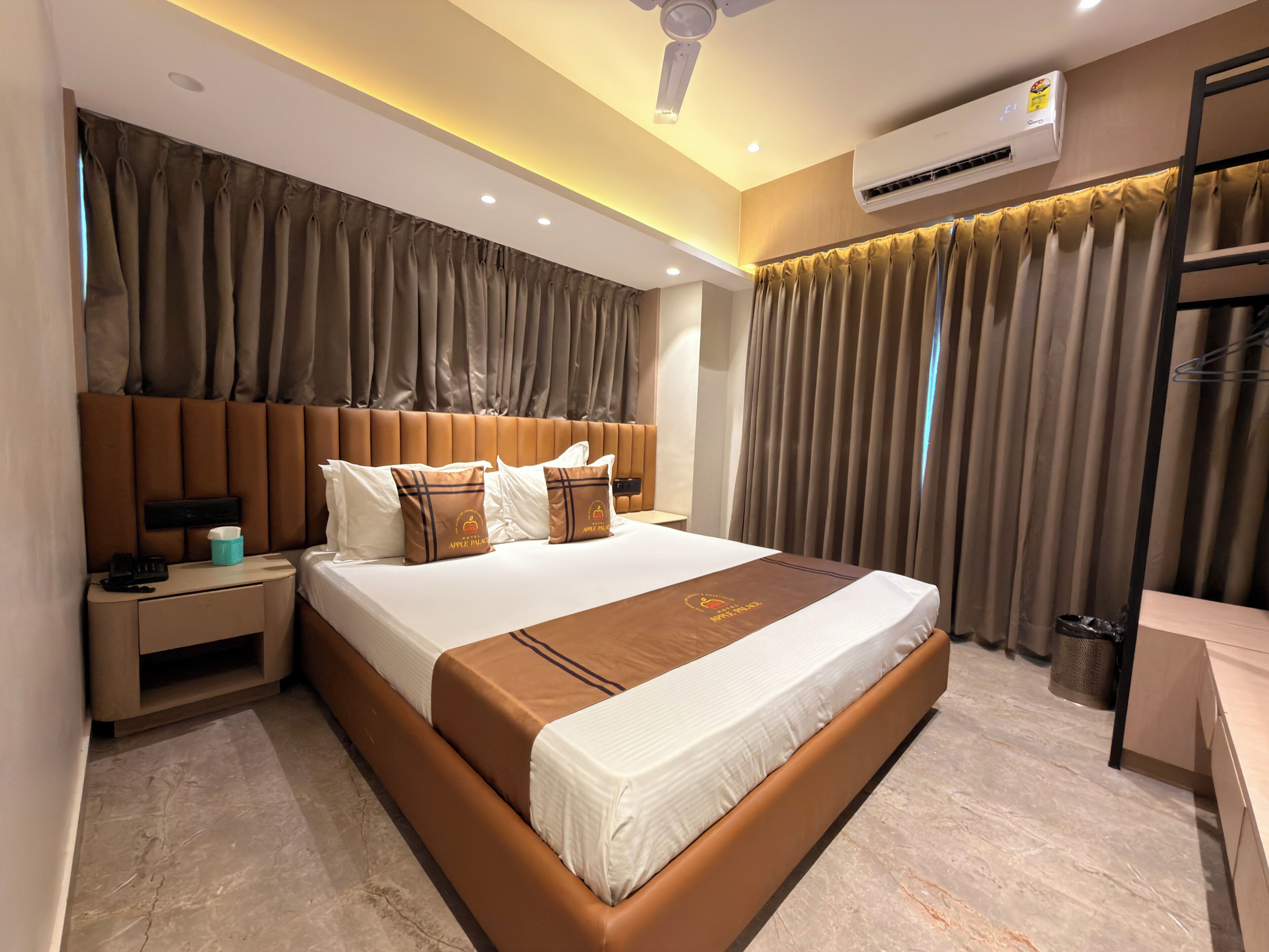 Una habitación de hotel con una cama grande, una mesita de noche, un equipo de aire acondicionado y un ventilador de techo.