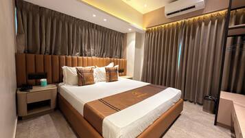 Una habitación de hotel con una cama grande, una mesita de noche, un equipo de aire acondicionado y un ventilador de techo.