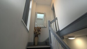 Eine enge Treppe mit Handlauf, einem Wandspiegel und einer Vase mit Trockenblumen.