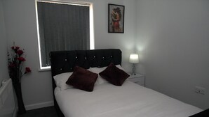 Ein ordentlich bezogenes Bett mit zwei Kissen, einer Nachttischlampe und einem gerahmten Bild an der Wand.
