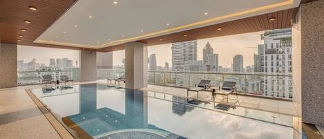 Una piscina infinita en la azotea con vistas a la ciudad, sillas de descanso y un diseño moderno.