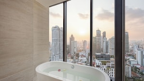 Un bagno moderno con una vasca da bagno grande, vista sulla città attraverso finestre a tutta altezza e una parete rivestita in piastrelle.