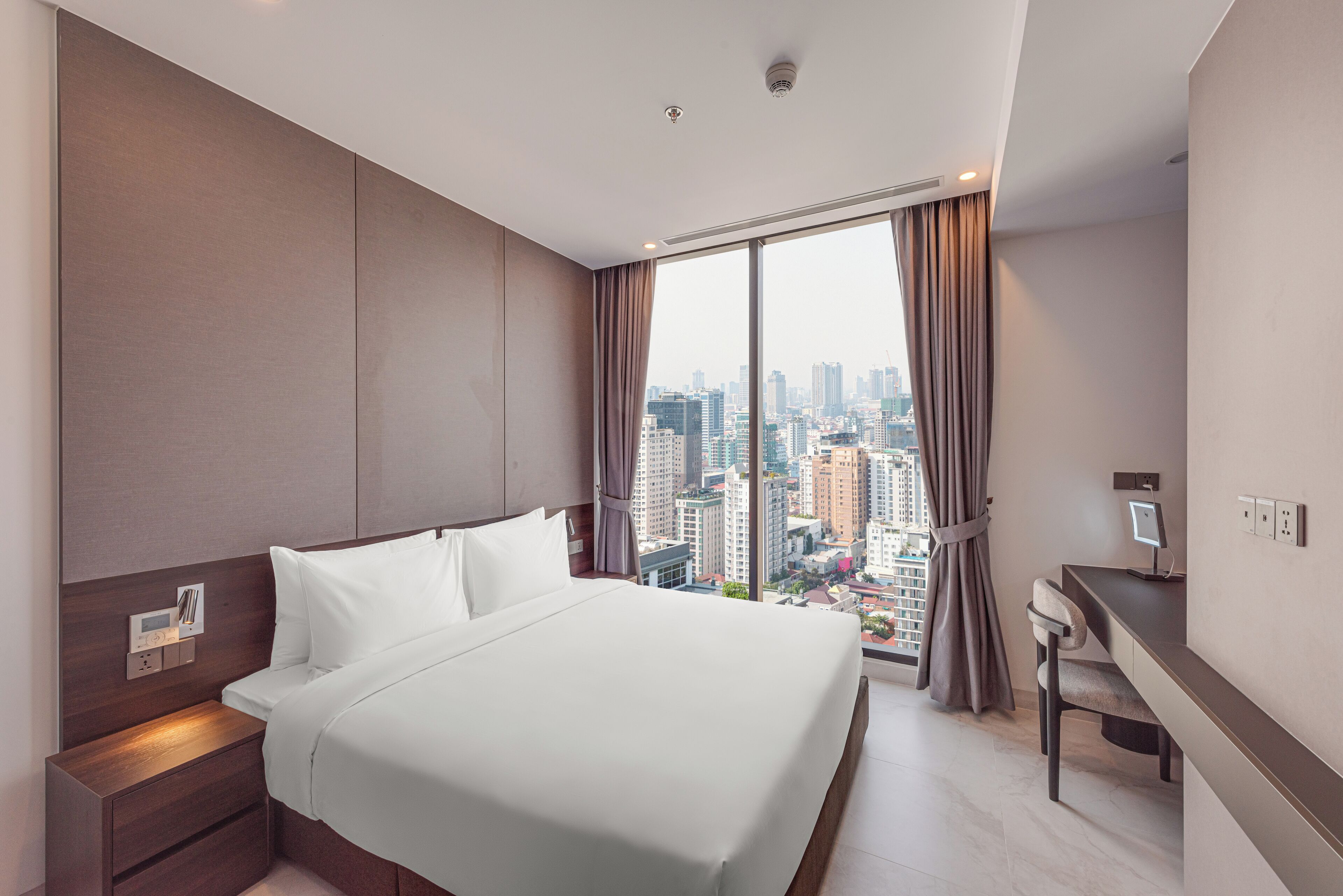 A modern hotel room with a large bed, a desk, and a city view.