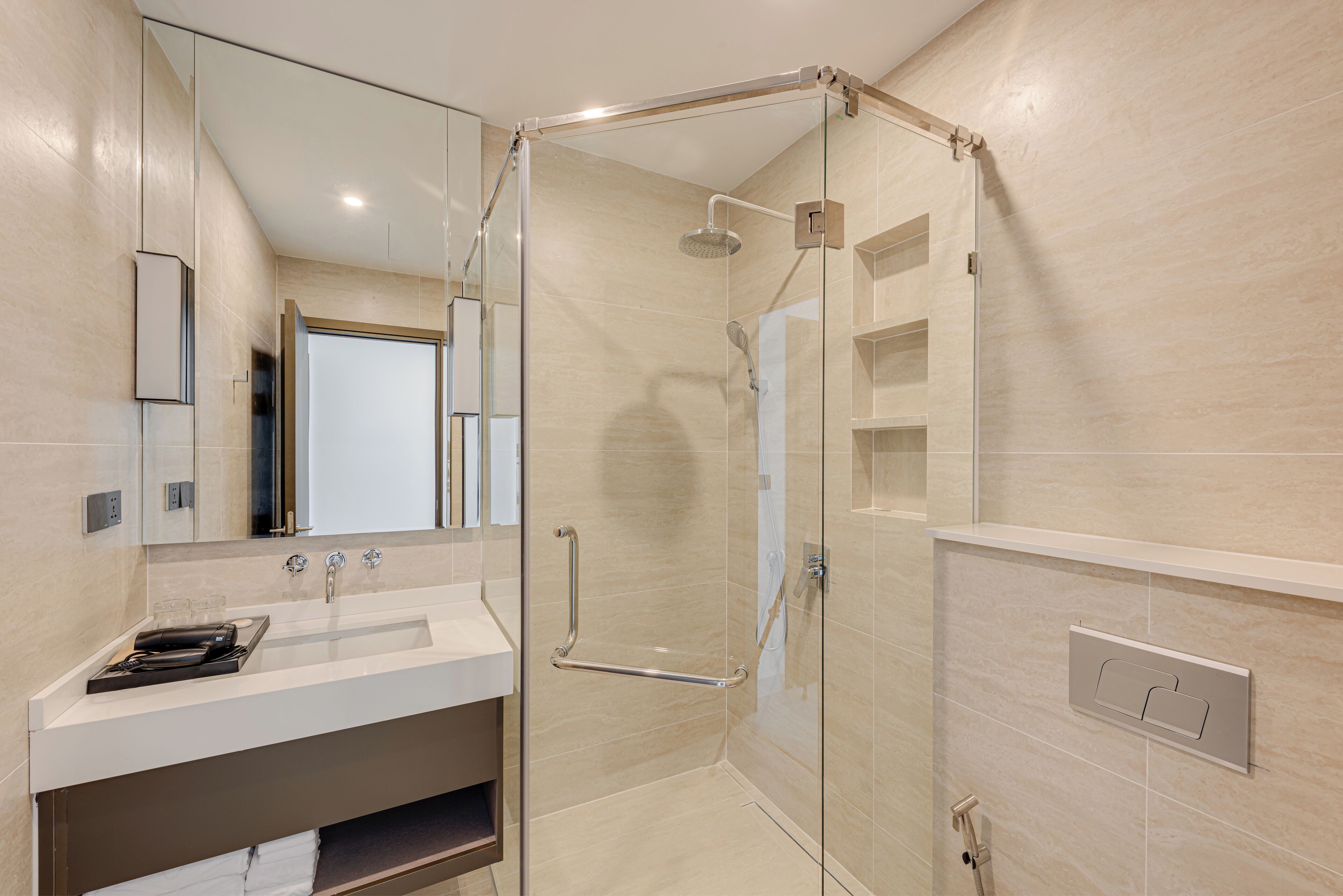 Un baño moderno con ducha envuelta en vidrio, tocador con lavamanos y espejo.