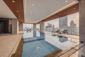 A modern indoor swimming pool with a city view, wooden ceiling, and lounge chairs. - Grand Mansion (Phnom Penh)