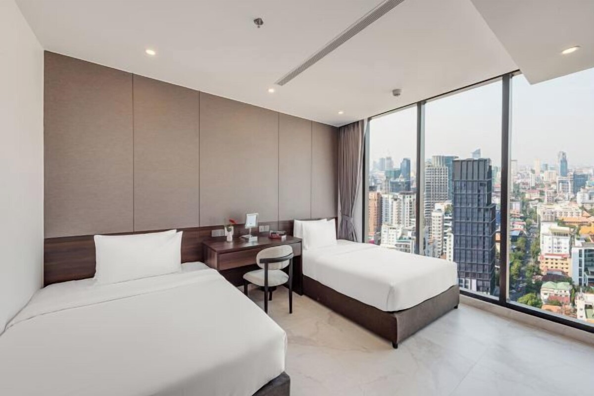 Quarto de hotel moderno com duas camas, uma escrivaninha e uma cadeira.