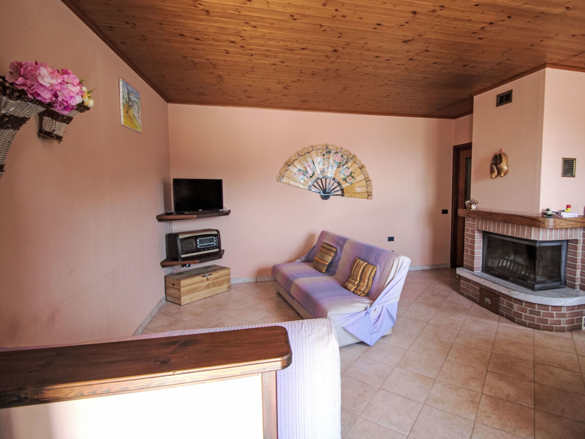 A cozy living room with a wooden ceiling, a sofa, a television, a fireplace, and a decorative fan.