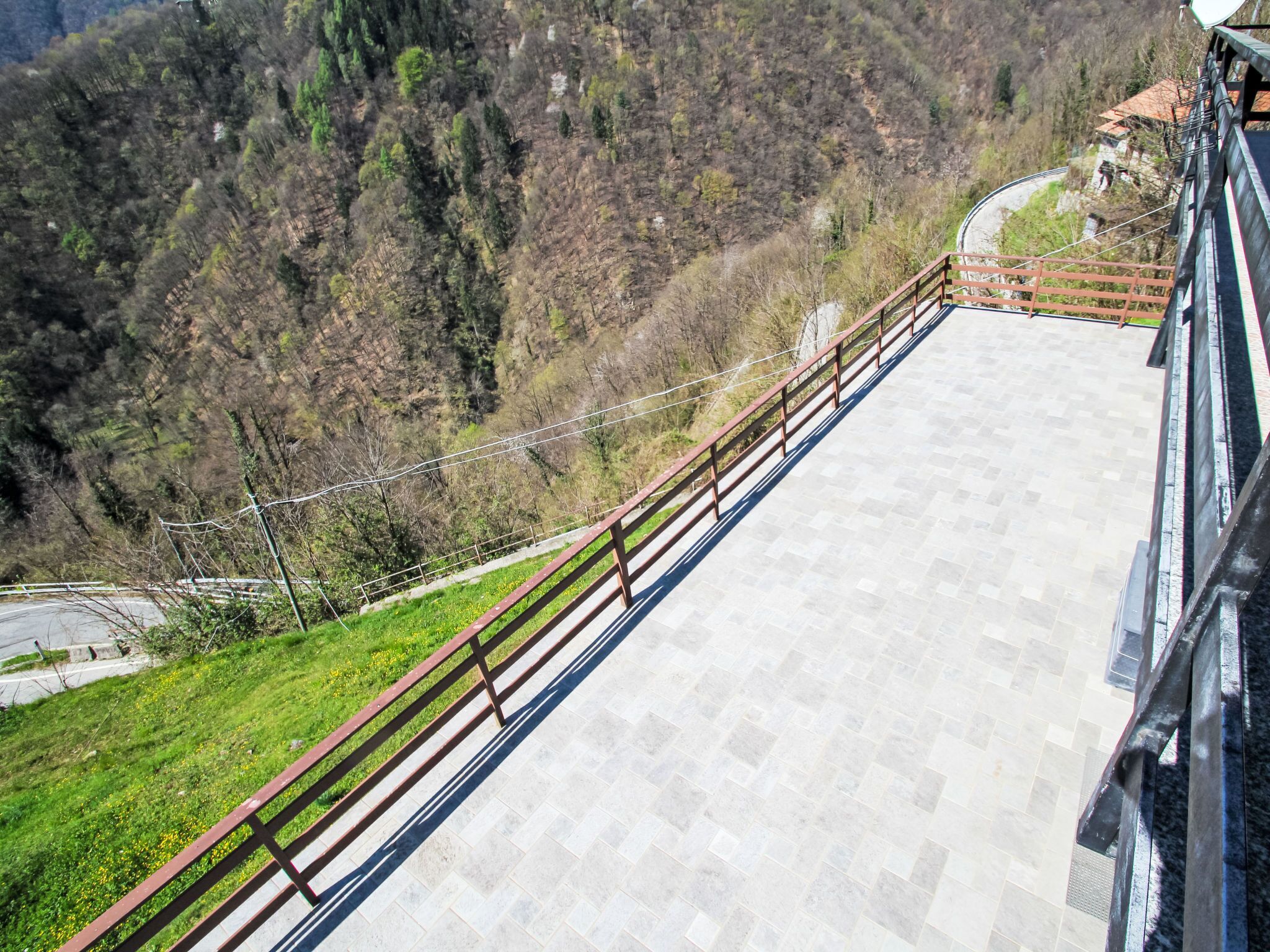 Vista panorâmica de um ponto elevado, com paisagem montanhosa, calçada pavimentada e guarda-corpo de madeira.