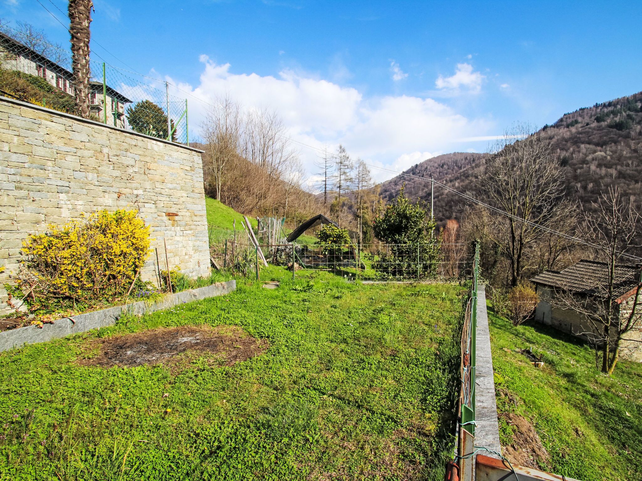 Paisatge rural amb una paret de pedra, una petita casa de fusta i un camp de gespa.