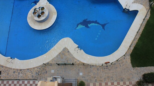 An aerial view of a swimming pool with a unique wavy edge design, surrounded by a stone and tiled deck area. - Wonderful apartment at Ronda IV Fuengirola (Fuengirola)