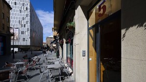 Une rue avec des tables en terrasse, un bâtiment portant le chiffre « 5 » et, au fond, un immeuble moderne.