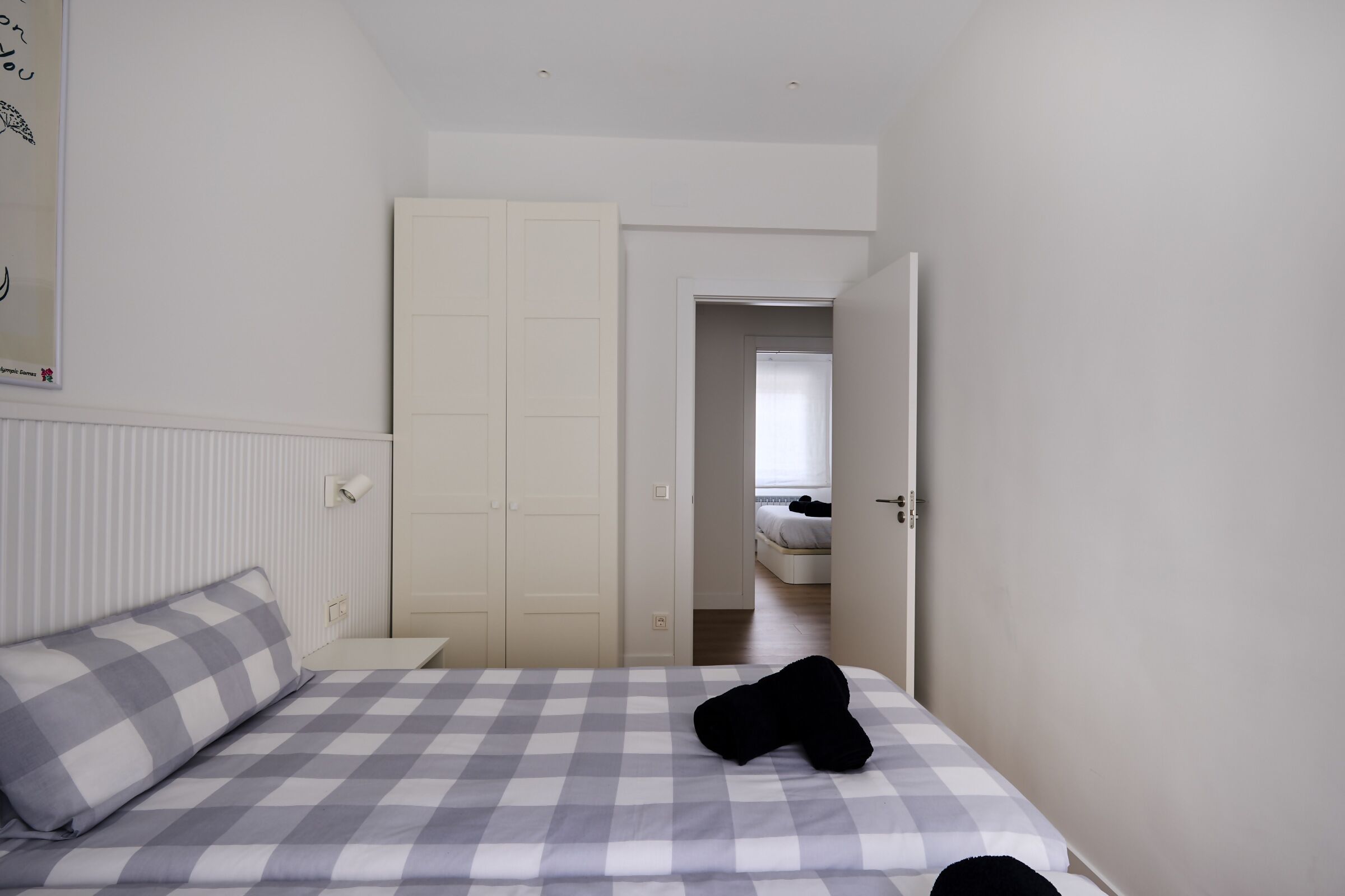 A bedroom with a checkered bedspread, a white door, and a view into another room.