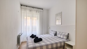Une chambre à coucher avec une couvre-lit à carreaux, un radiateur, une table de chevet et une fenêtre ornée de rideaux légers.