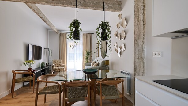 Une cuisine moderne avec une table à manger en verre, des chaises en bois, des plantes suspendues et un réfrigérateur blanc.