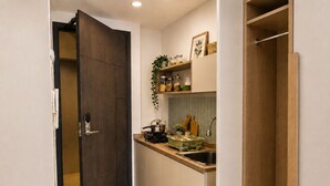 Une cuisine moderne avec une porte en bois foncé, des armoires blanches, un évier en acier inoxydable et un plan de travail sur lequel sont disposés divers ustensiles de cuisine.