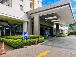 A modern building entrance with a clear pedestrian path marked by a sign, a parking area, and a well-maintained hedge.