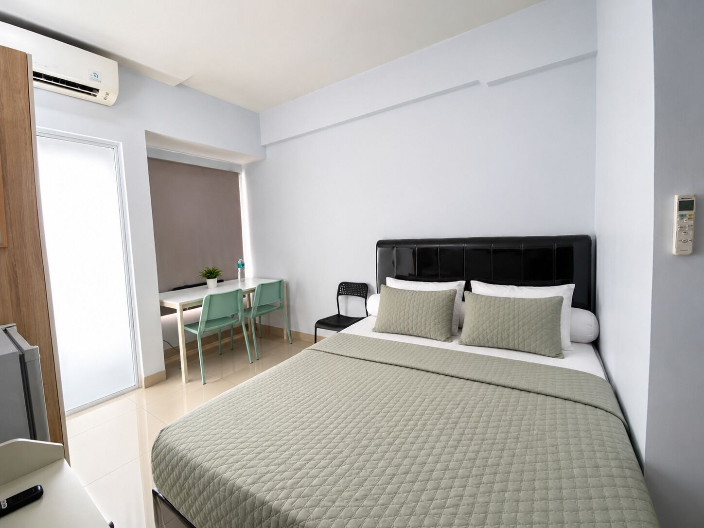 A modern bedroom with a bed, bedside table, and a desk area with chairs.