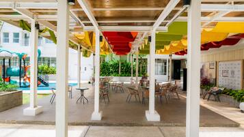 An indoor patio area with tables and chairs, a pool, and a playground with colorful equipment.