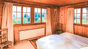 A wooden cabin bedroom with a bed, a chair, a radiator, and large windows. - La Capsule by Interhome (Thyon-Les Collons)