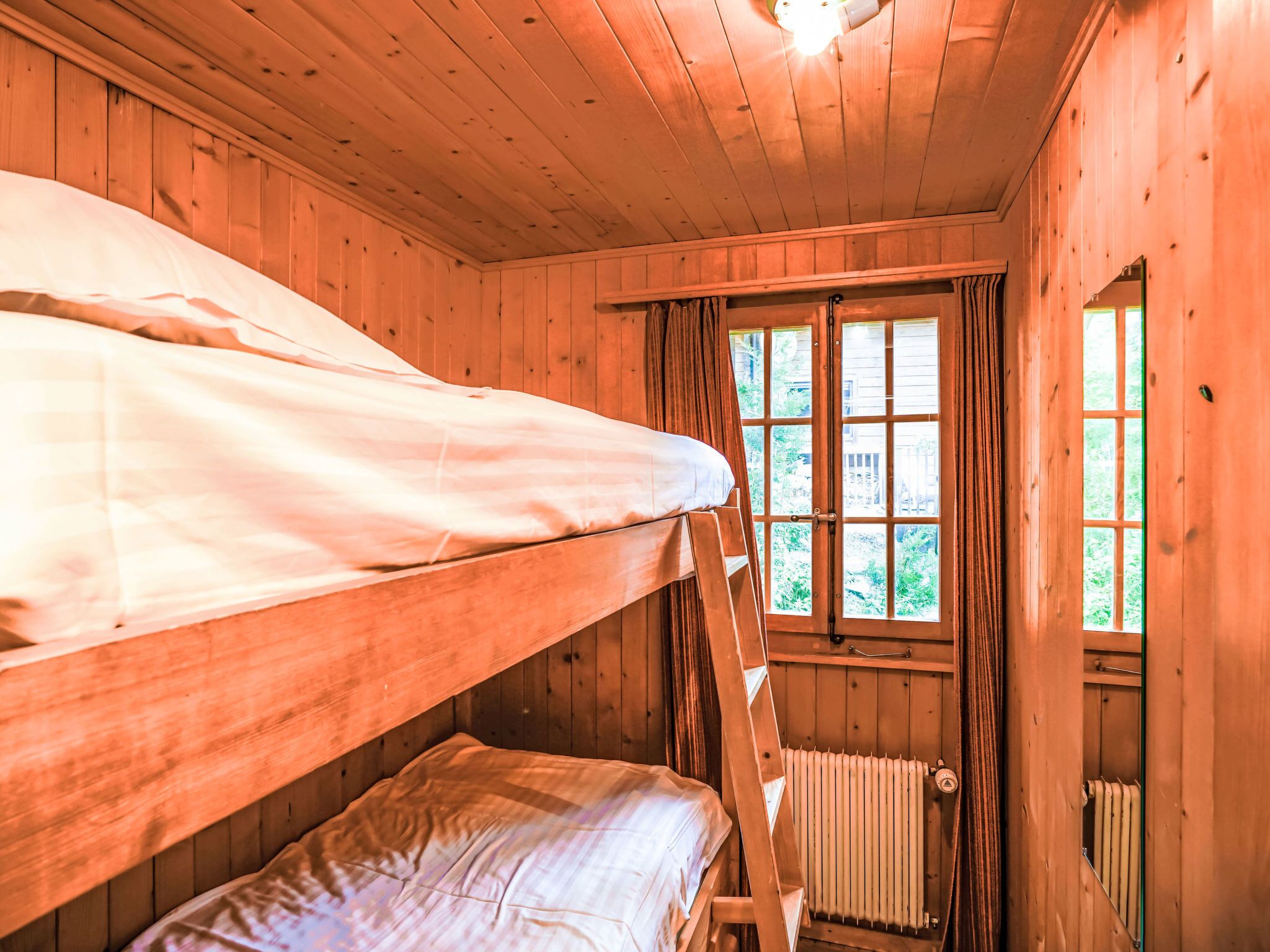Una habitación tipo cabaña con literas, una ventana con cortinas y un radiador.