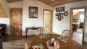 A dining area with a wooden table, chairs, and a ceiling fan. There is a wooden door and a framed picture on the wall.