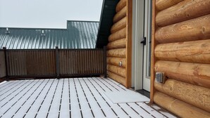 A wooden cabin with a snow-covered deck and a metal roof.