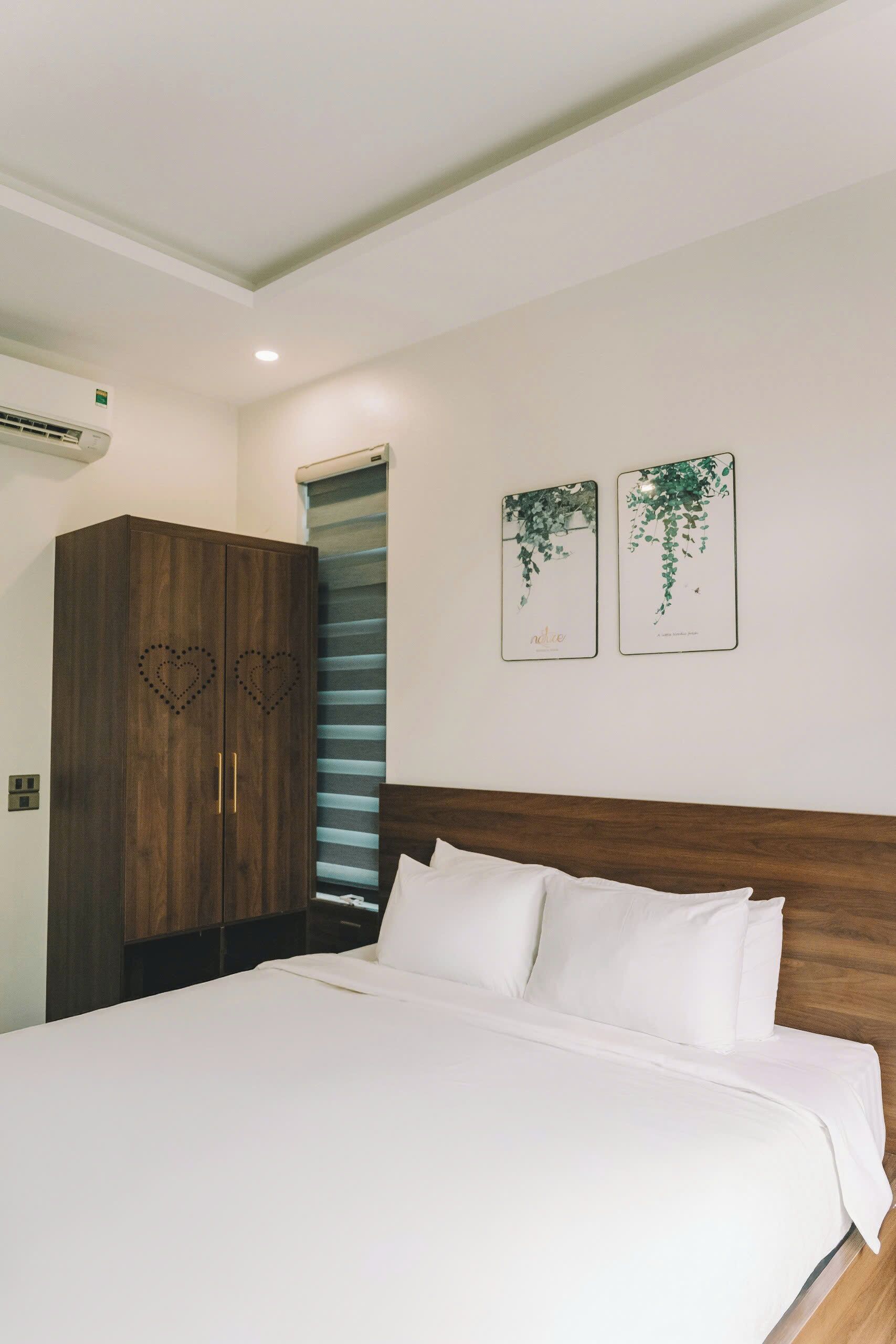 A bedroom with a large bed, wooden wardrobe, and two wall-mounted pictures.