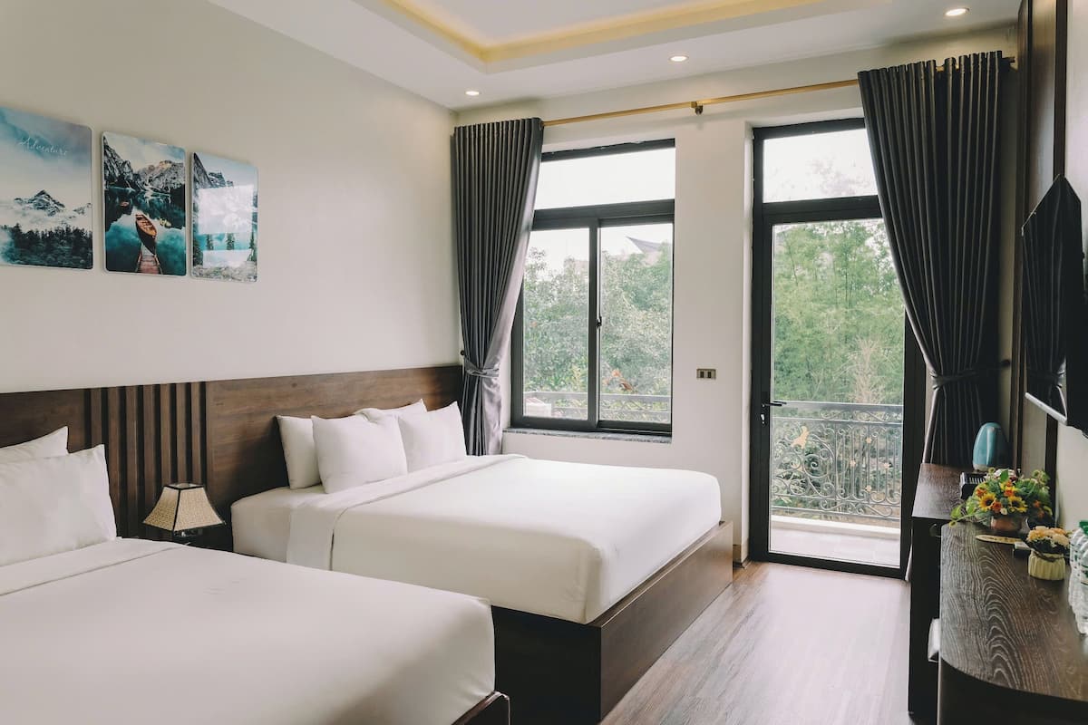 Een hotelkamer met twee bedden, een groot raam met gordijnen, een houten hoofdbord en een tafeltje met een bloevas.
