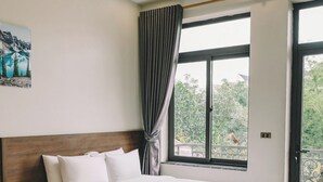 Une chambre d’hôtel moderne avec un grand lit, un lit plus petit et un balcon donnant sur un paysage verdoyant.