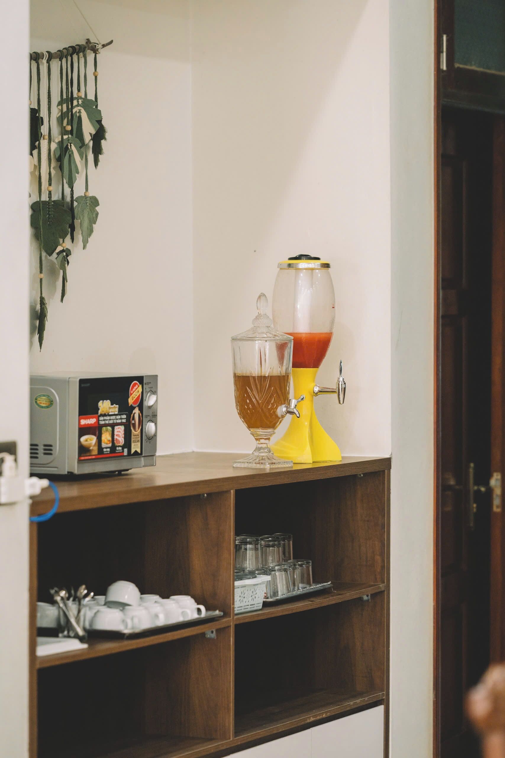 A kitchen area with a coffee maker, a glass carafe, and a microwave on a wooden shelf.