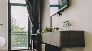 Une chambre d’hôtel moderne avec un plancher en bois, un grand téléviseur fixé au mur, un balcon avec vue et un petit bureau agrémenté d’un vase de fleurs.