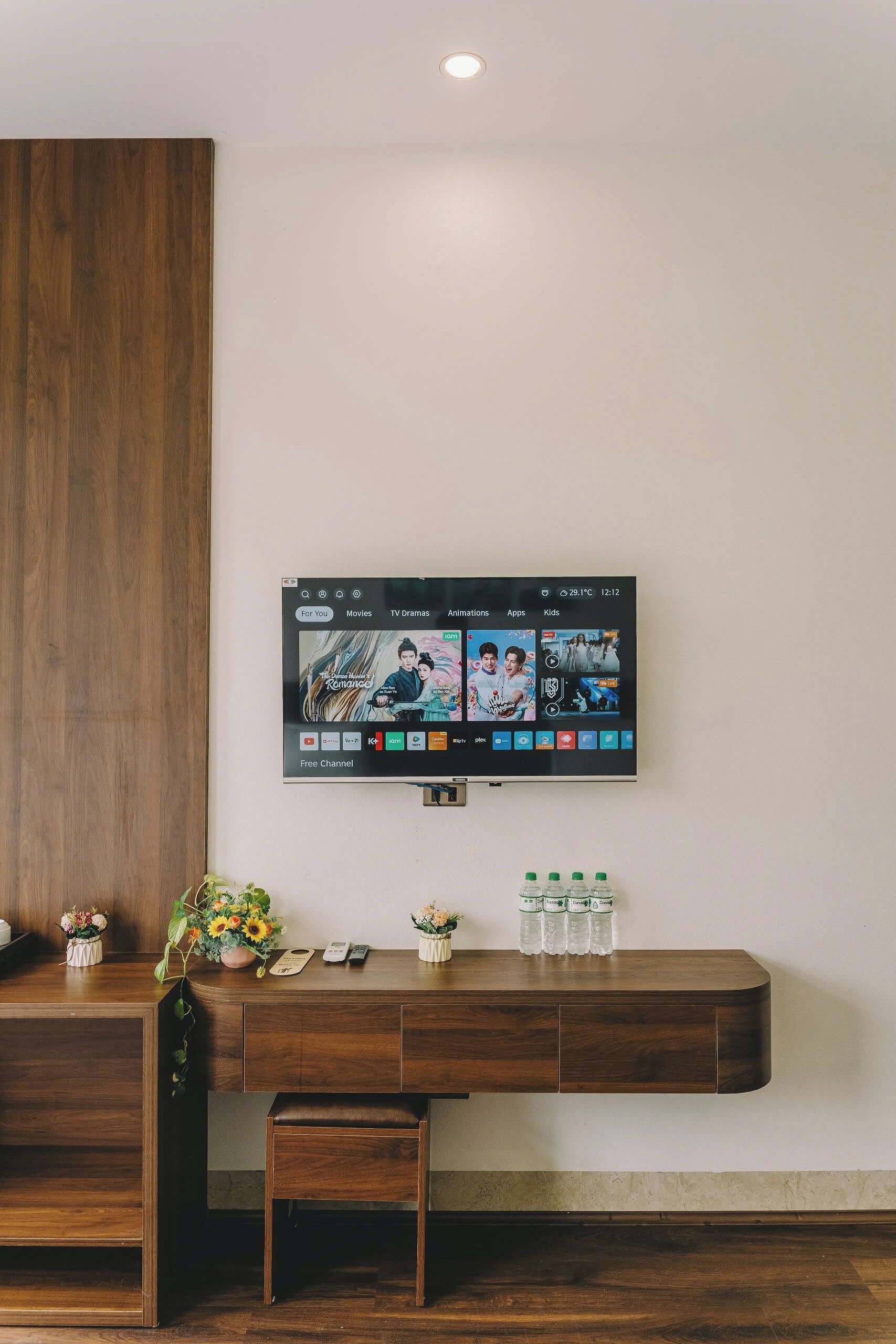 A modern room with a wooden desk, a mounted TV displaying various streaming options, and a small bench.