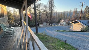 A wooden deck with outdoor seating, a covered area, and a view of a gravel path leading to a house with a small shed. - Yosemite Sky Getaway - Newly Remodeled, 2 King Beds, EV Charger, RV/Boat Parking (Oakhurst)