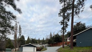 A gravel driveway leading to a garage with a covered area, surrounded by trees and a wooden fence. - Yosemite Sky Getaway - Newly Remodeled, 2 King Beds, EV Charger, RV/Boat Parking (Oakhurst)