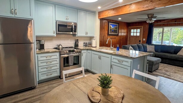 A modern kitchen with light blue cabinets, stainless steel appliances, and a wooden dining table with a plant centerpiece. - Yosemite Sky Getaway - Newly Remodeled, 2 King Beds, EV Charger, RV/Boat Parking (Oakhurst)