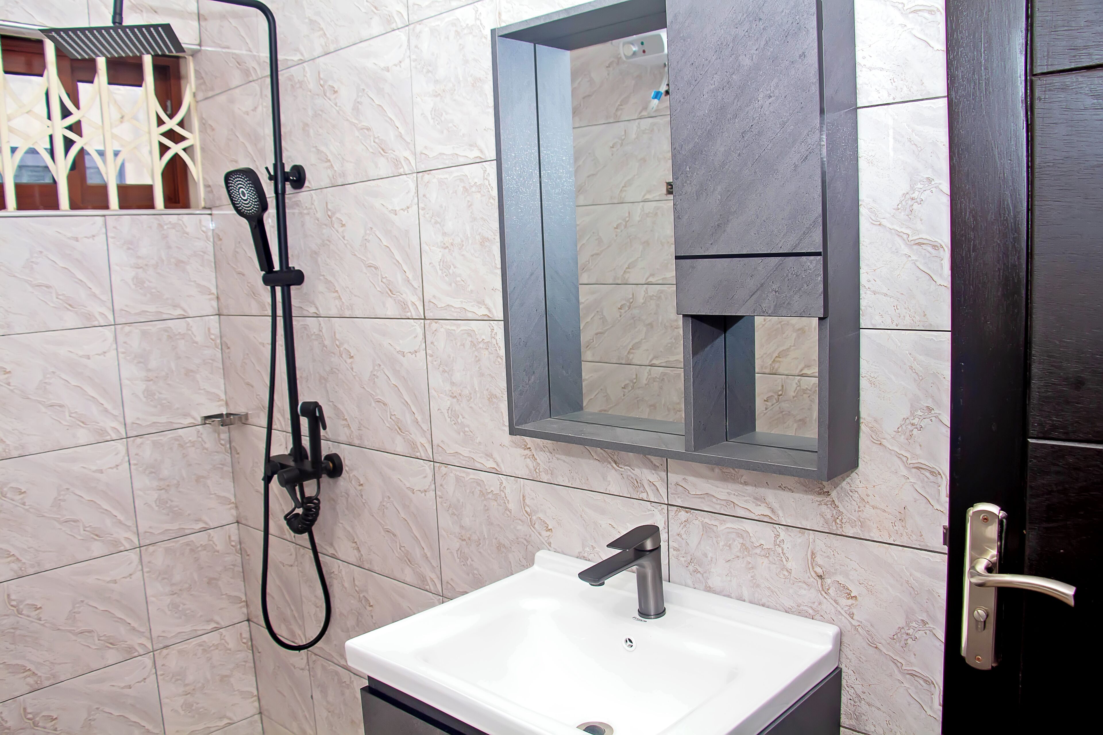 Une salle de bain avec un lavabo blanc, une douchette à main et un miroir doté d’un cadre en bois.