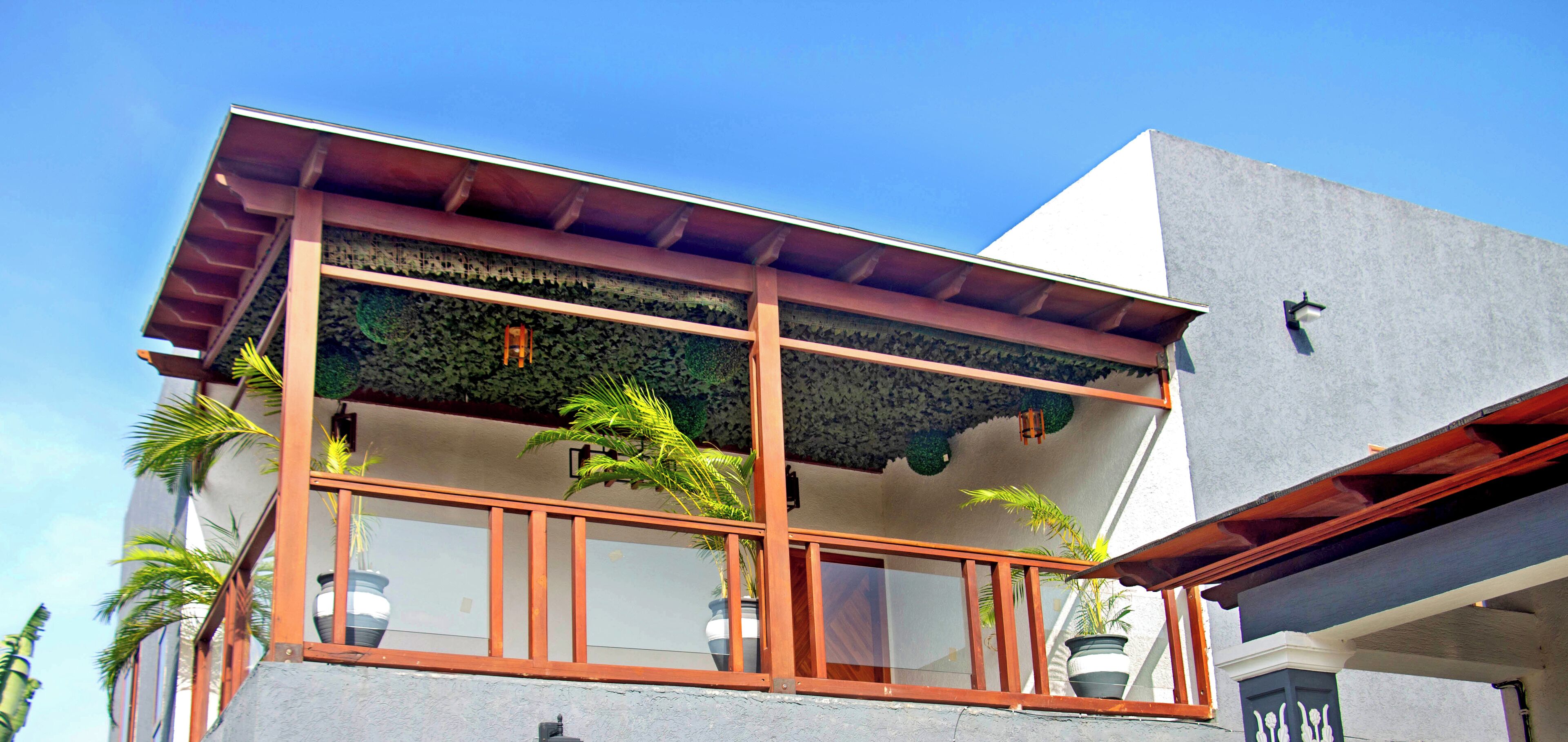 A two-story building with a balcony, potted plants, and a clear blue sky.