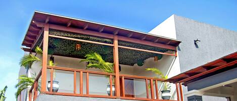 A two-story building with a balcony, potted plants, and a clear blue sky.