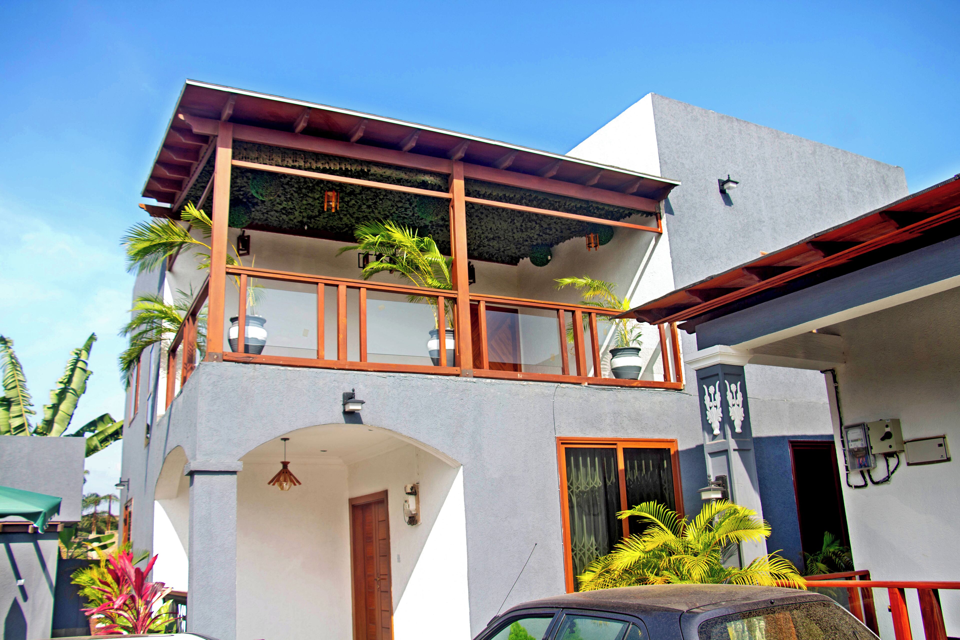 A two-story building with a balcony, a car parked in front, and a clear blue sky.