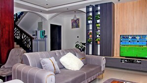 A modern living room with a grey sofa, a wooden coffee table, and a TV displaying a sports game. - Royal Tulip Court (Accra)
