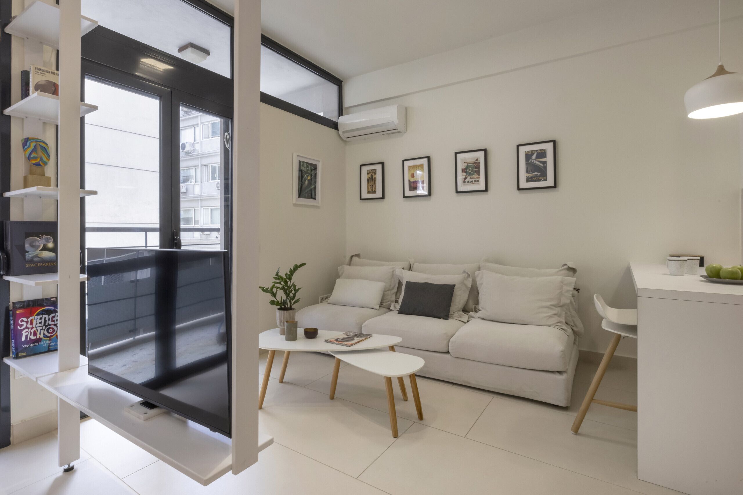 A modern living room with a sofa, a coffee table, and a TV. There are framed pictures on the wall and a balcony with a view.