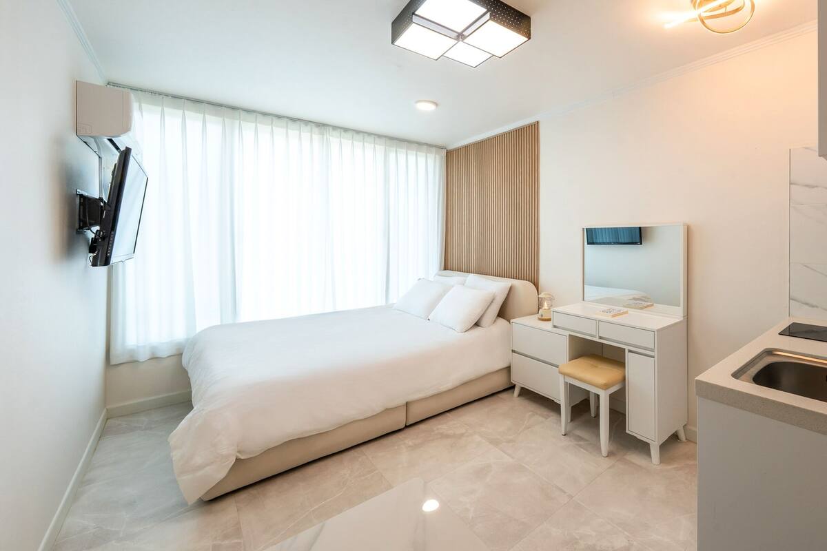 A modern hotel room with a bed, desk, and built-in sink.