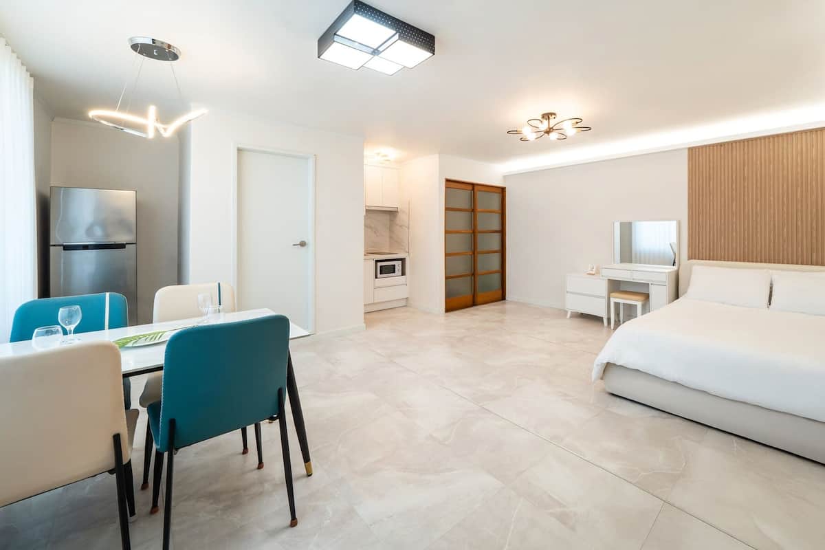 A modern hotel room with a dining area, kitchenette, and a large bed.