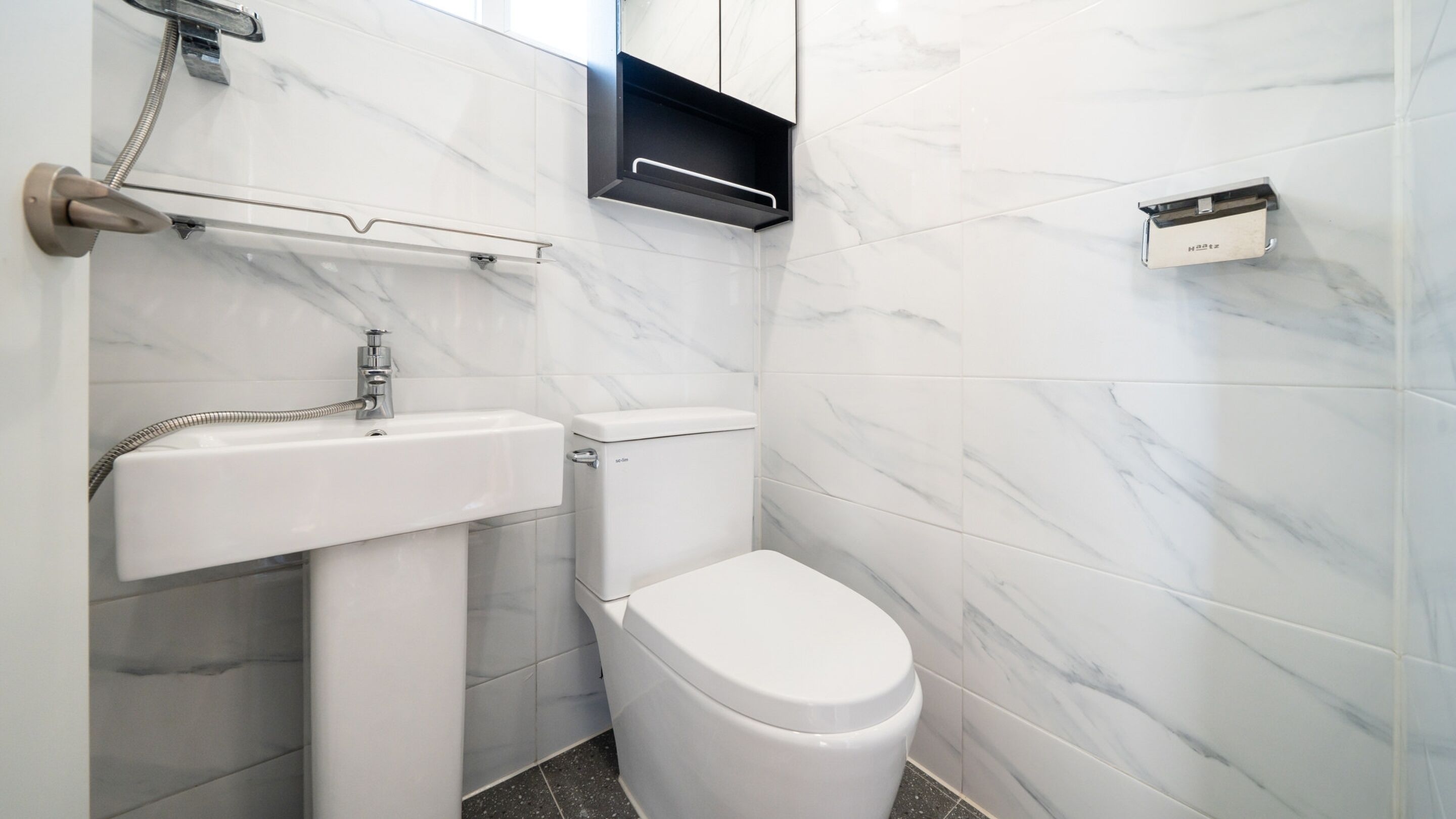 Une petite salle de bain avec des toilettes blanches, un lavabo sur colonne et un porte-serviettes.