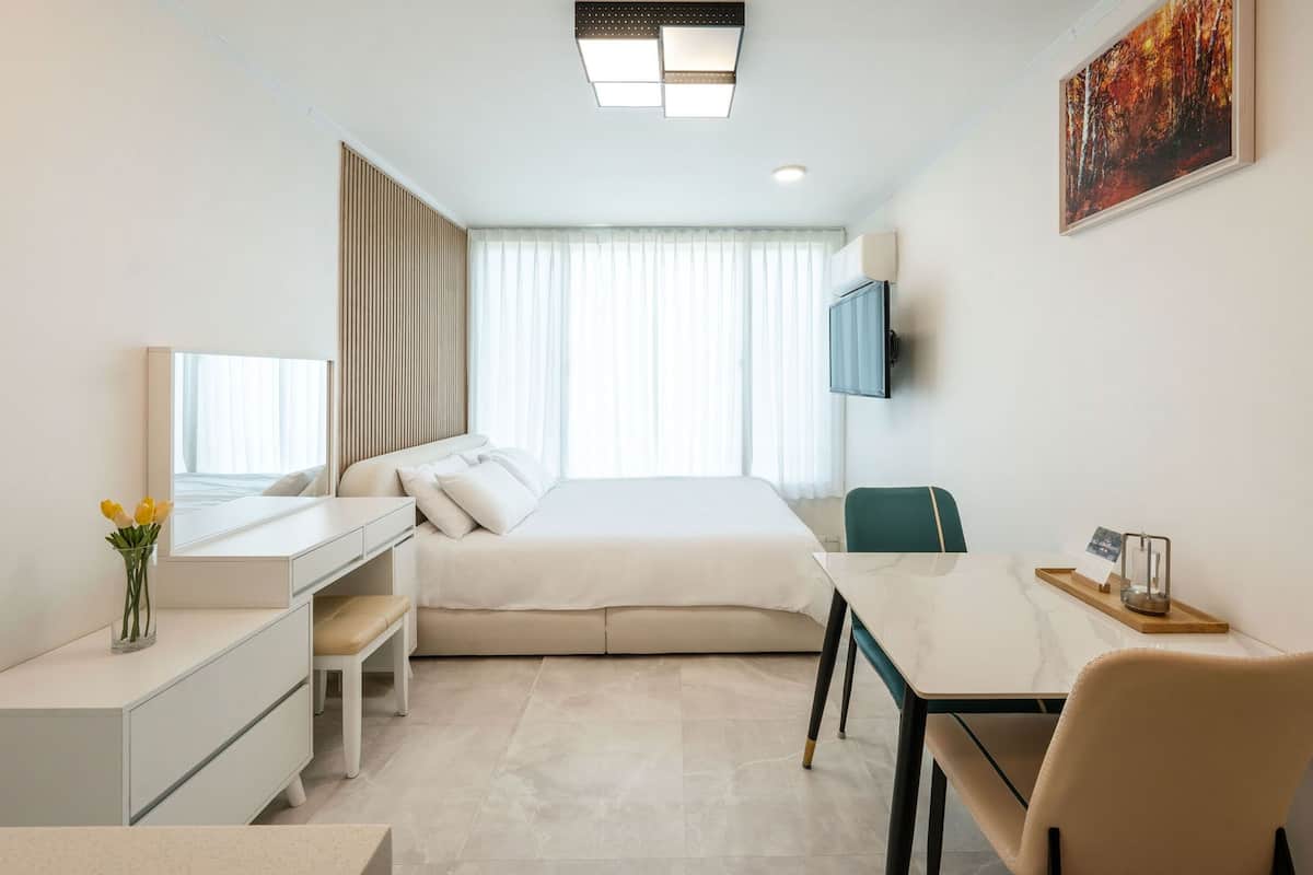 A modern hotel room with a bed, a desk, a chair, a TV, and a painting on the wall.