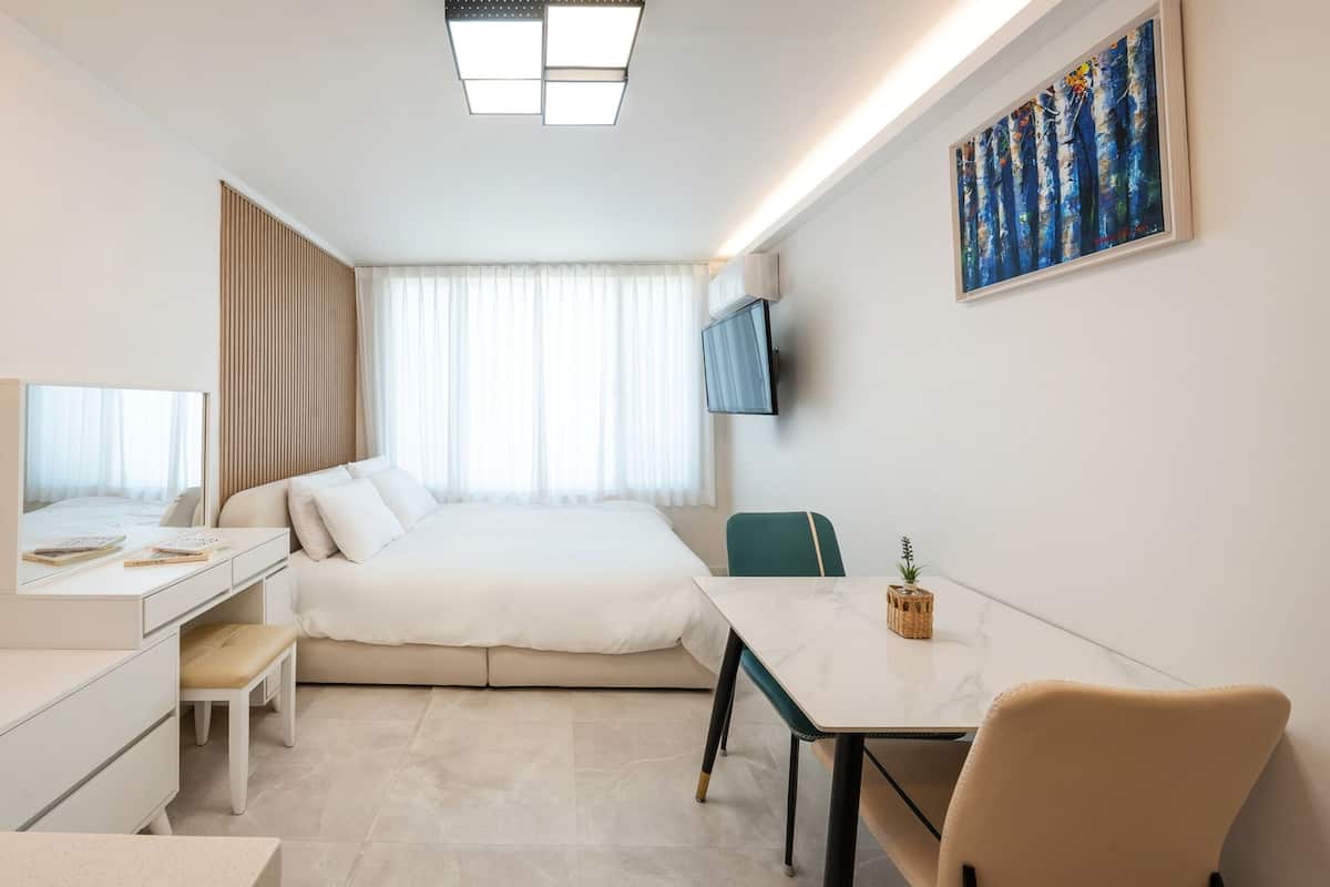 A modern hotel room with a bed, a desk, a chair, a TV, and a painting on the wall.