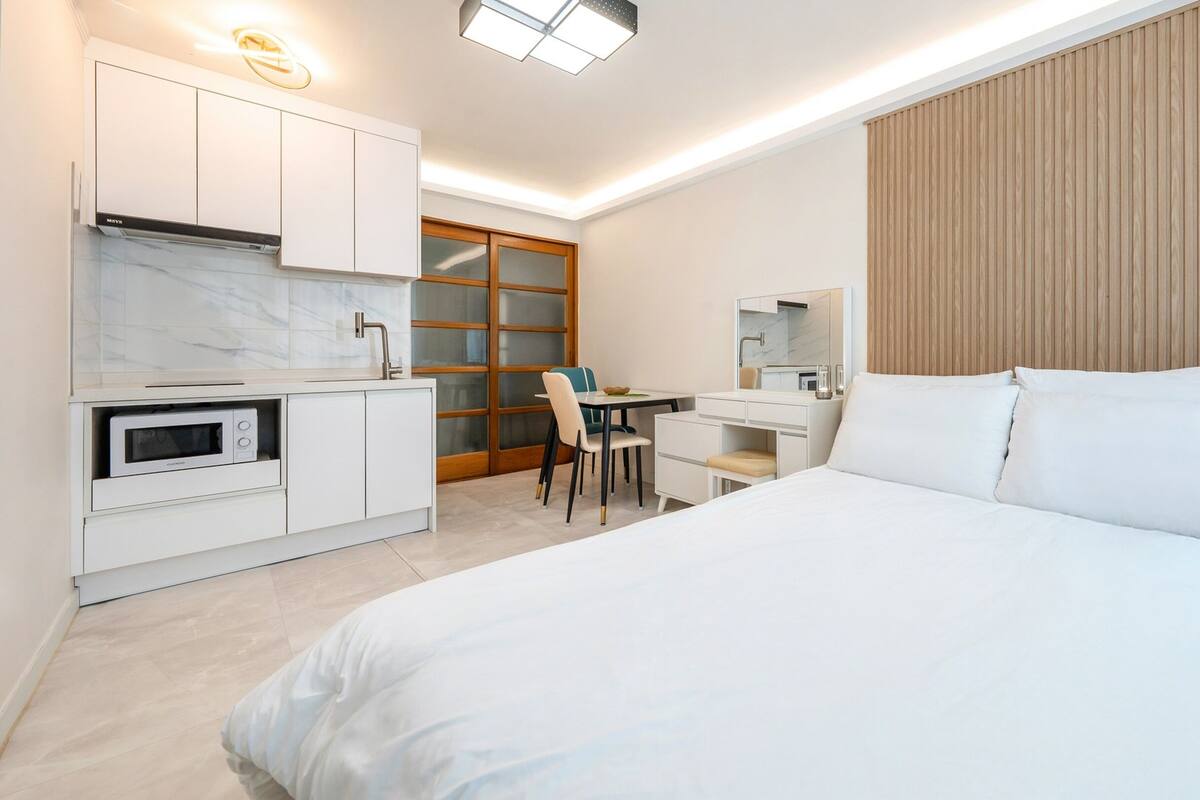 A modern hotel room with a bed, a desk, a microwave, and a large window with blinds.