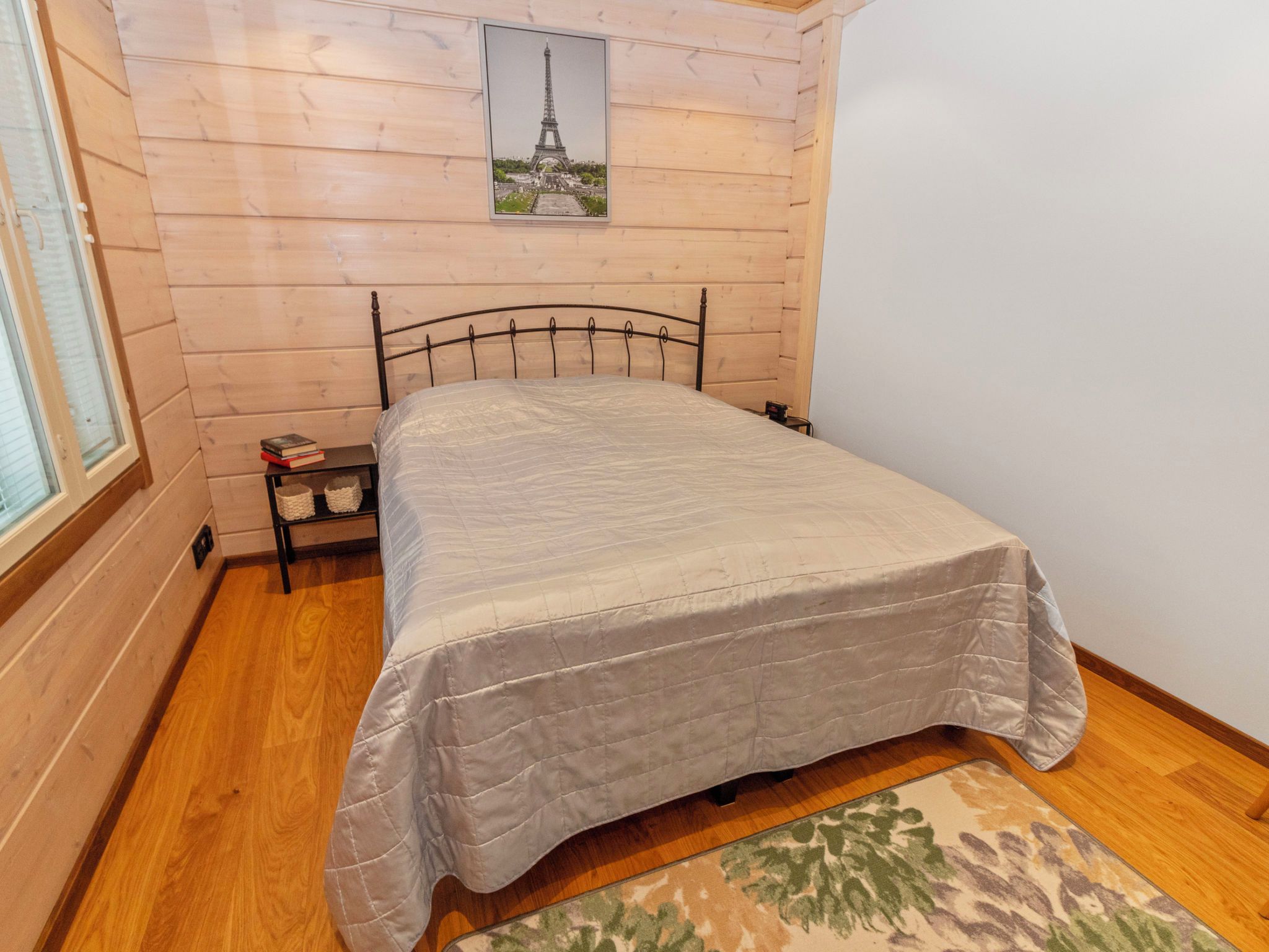 Quarto com cama, mesa de cabeceira, quadro emoldurado da Torre Eiffel, paredes de madeira e janela.