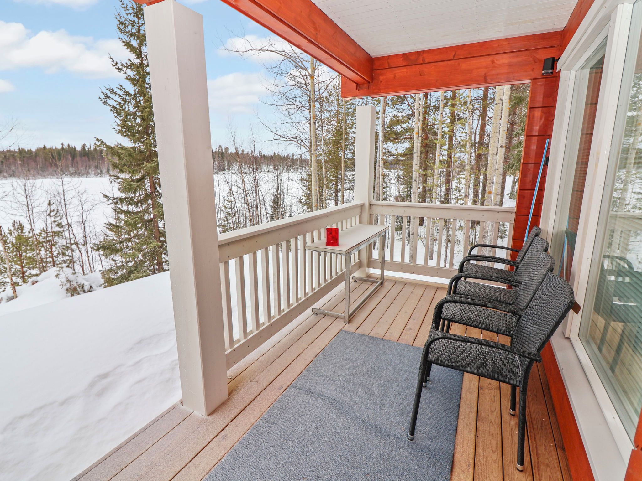 A wooden deck with a railing, a gray mat, and three wicker chairs.